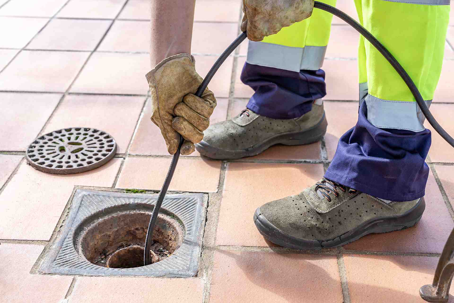 Man cleaning the floor drain in a commercial kitchen with hot water jetting machine