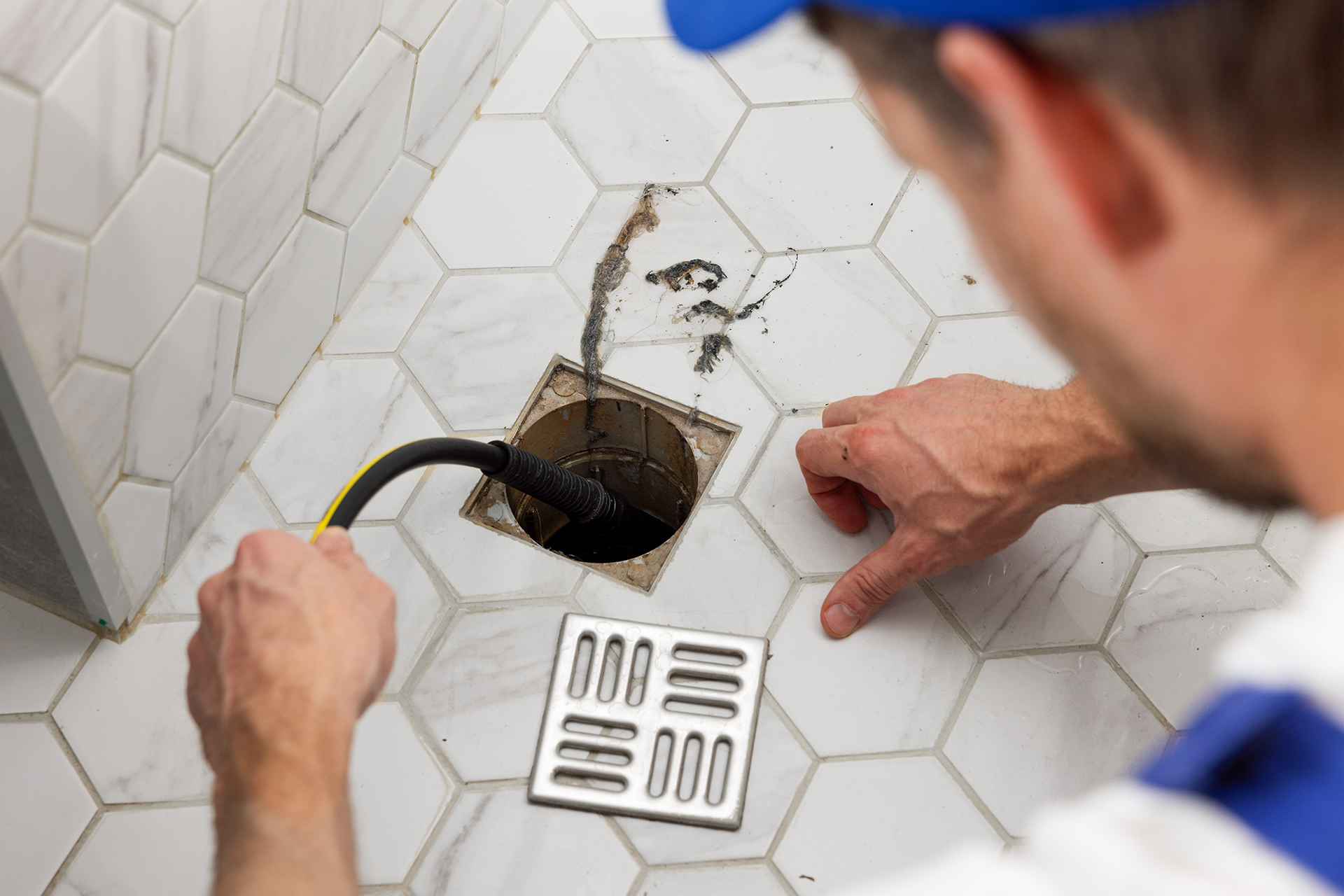 Man cleaning the floor drain in a bathroom with hot water jetting machine