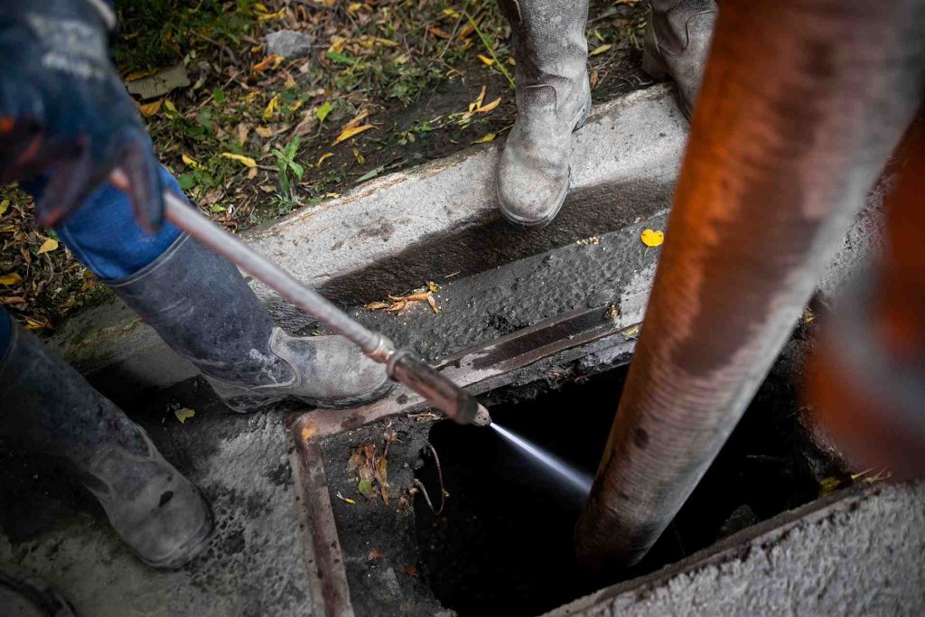 Workers cleaning sewer drain with hot water jet
