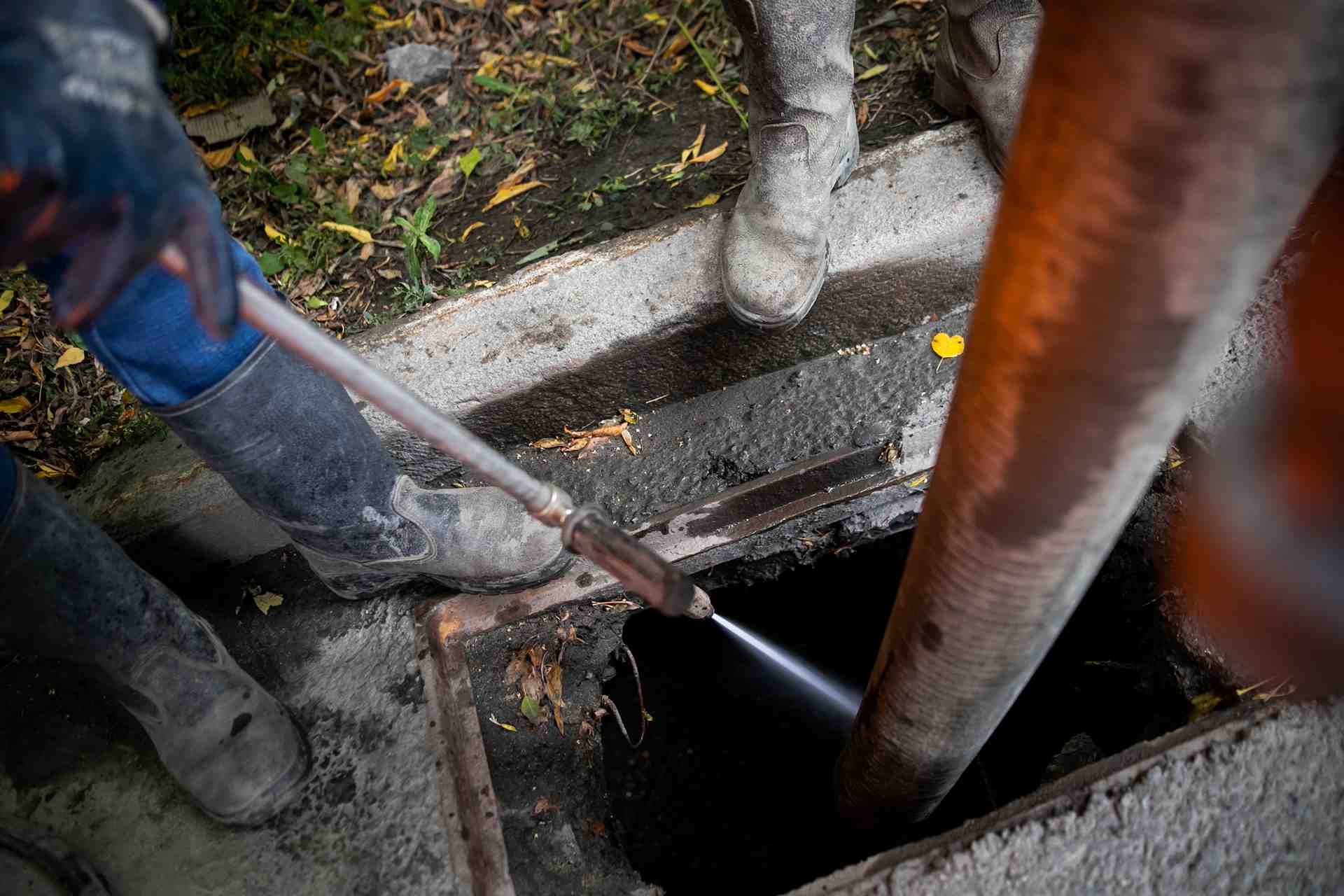 Workers cleaning sewer drain with hot water jet