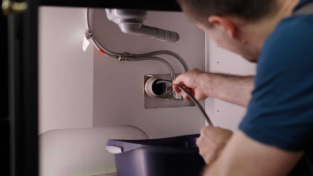 Man cleaning sink drain with hot water jetting machine